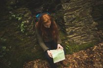 Рыжеволосая женщина-туристка с рюкзаком читает карту в лесу — стоковое фото