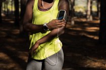 Metà sezione di atleta femminile ascoltare musica da smartphone lettore mp3 — Foto stock