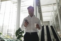 Hombre de negocios sonriente revisando su teléfono en la oficina - foto de stock