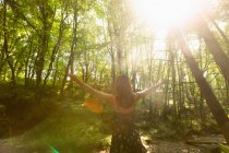 Вид ззаду жінки, що стоїть в лісі з розкиданими руками — стокове фото