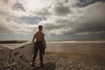 Серфер с доской для серфинга смотрит на море с пляжа в солнечный день — стоковое фото