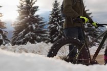 Homem de pé com bicicleta em uma paisagem nevada durante o inverno . — Fotografia de Stock
