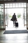 Vue arrière de la femme avec sac trolley quittant l'hôtel — Photo de stock