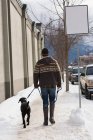Чоловік ходить з собакою на тротуарі взимку . — стокове фото