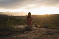 Rückansicht einer Frau, die auf einem Felsen sitzt und die Natur betrachtet — Stockfoto