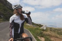 Female biker drinking water from bottle on road on a sunny day — Stock Photo