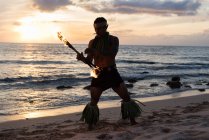 Male fire dancer performing with fire levi stick at beach — Stock Photo