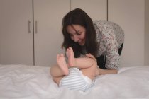 Усміхнена молода мати грає з дитиною в спальні вдома — стокове фото