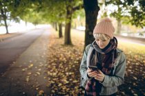 Молодая женщина в теплой одежде пользуется мобильным телефоном в парке — стоковое фото