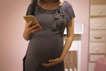 Schwangere berührt ihren Bauch, während sie Handy im Geschäft benutzt — Stockfoto
