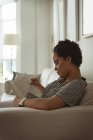 Frau liest zu Hause ein Buch auf Sofa — Stockfoto