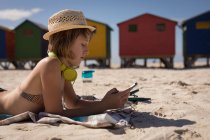 Дівчина-підліток використовує мобільний телефон, відпочиваючи на пляжі в сонячний день — стокове фото