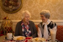 Amigos mayores interactuando brujas mientras desayunan en casa - foto de stock