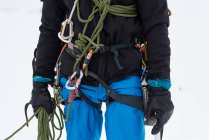 Alpinista maschio in piedi con corda e imbracatura su una regione innevata — Foto stock