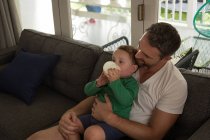 Padre guardando suo figlio bere latte in soggiorno a casa — Foto stock