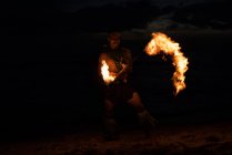 Male fire dancer performing with burning fire levi stick on beach at night — Stock Photo