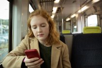 Mujer joven pelirroja usando su móvil en tren - foto de stock