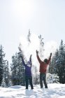 Casal jogando neve no ar em bosques nevados em montanhas . — Fotografia de Stock