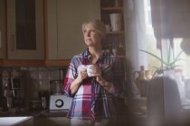 Задумчивая зрелая женщина пьет кофе на кухне дома — стоковое фото