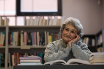 Mujer mayor reflexiva sonriendo en la biblioteca - foto de stock
