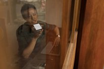 Homme d'affaires parlant sur téléphone portable dans un café derrière une vitre — Photo de stock