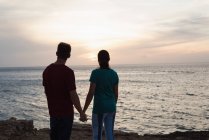Silhueta de casal de mãos dadas na praia ao pôr do sol — Fotografia de Stock