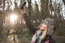 Donna bionda che si fa selfie con il cellulare nella foresta . — Foto stock