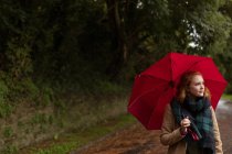 Giovane donna in piedi con ombrello nel parco — Foto stock