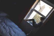 Livre de lecture femme sur rebord de fenêtre dans la chambre à coucher à la maison — Photo de stock