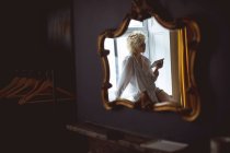 Spiegelung der Frau mit digitalem Tablet in der Nähe des Fensters im Spiegel zu Hause — Stockfoto