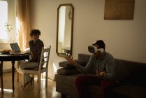 Жінка дивиться на чоловіка, використовуючи гарнітуру віртуальної реальності у вітальні — стокове фото