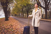 Femme d'affaires avec bagages debout dans la rue pendant l'automne — Photo de stock