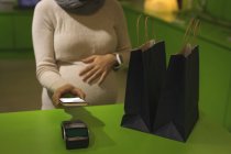 Femme enceinte effectuant le paiement par téléphone portable en magasin — Photo de stock