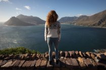 Visão traseira da mulher olhando para o lago e montanhas à luz do sol — Fotografia de Stock