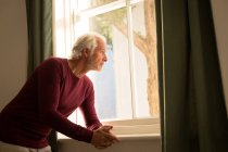 Продуманий старший чоловік дивиться через вікно на дому — стокове фото