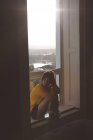 Задумчивая женщина отдыхает у окна дома — стоковое фото