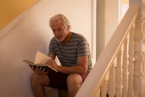 Uomo anziano attivo che legge un libro sulle scale a casa — Foto stock
