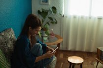 Frau benutzt Handy auf Sofa im heimischen Wohnzimmer — Stockfoto