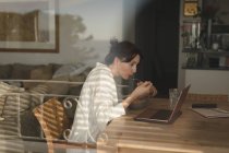 Молодая женщина ест завтрак, глядя в ноутбук в гостиной на дому — стоковое фото