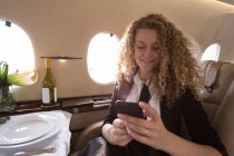 Mujer de negocios rubia usando el teléfono móvil en jet privado - foto de stock