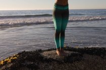 Partie basse de la femme en vêtements de sport sur le rocher à la plage au crépuscule
. — Photo de stock
