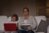 Бабуся і онука використовують ноутбук і цифровий планшет вдома — стокове фото
