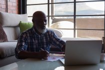 Старший чоловік перевіряє рахунки під час використання ноутбука вдома — стокове фото