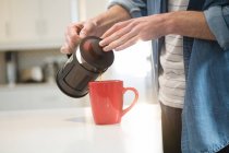 Середина чоловіка, що поливає каву з французької преси в кухоль в домашніх умовах — стокове фото