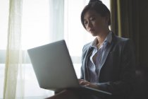 Donna d'affari che utilizza il computer portatile mentre seduto su una poltrona in camera d'albergo — Foto stock