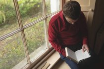 Человек, читающий книгу у окна дома — стоковое фото
