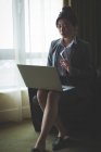Empresária usando laptop enquanto se senta na cadeira de braço no quarto do hotel — Fotografia de Stock