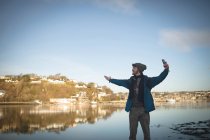 Мужчина-турист делает селфи с мобильным телефоном возле озера в сельской местности — стоковое фото