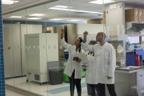 Científicos escribiendo nota en pared de vidrio en el laboratorio - foto de stock