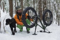 Homme avec chien réparant vélo en forêt pendant l'hiver . — Photo de stock